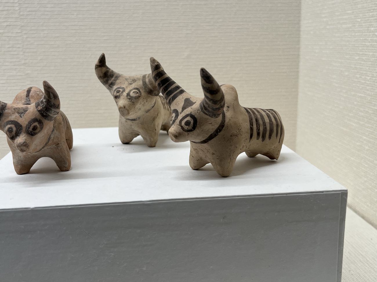 三体の小さな土製のコブウシ。目のまわりに黒い輪、角と体に黒い縞が描かれている。